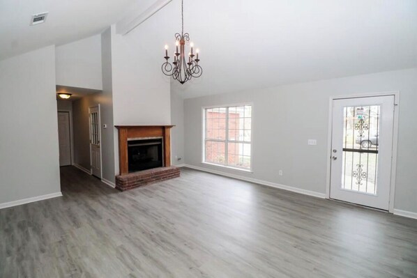 A spacious living room with hardwood flooring, a fireplace, a chandelier, and large windows.