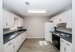 A kitchen with white cabinets, a black countertop, a stove, and a refrigerator.