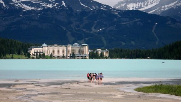 A hotel with a large building and multiple smaller structures, surrounded by mountains and a lake. - Gateway to Rocky Mountains -1 Bdr Suite/Kitchen/AC/UG Pk/Gym (Canmore)