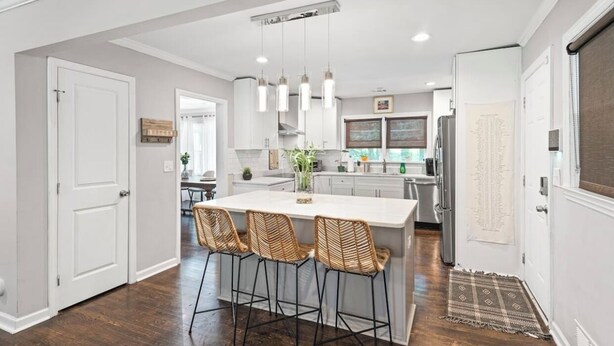 A modern kitchen with a central island, bar stools, pendant lighting, and a view into the dining area. - Spacious Luxurious Cozy Ranch Home - STRL-2022-00738 (Atlanta)