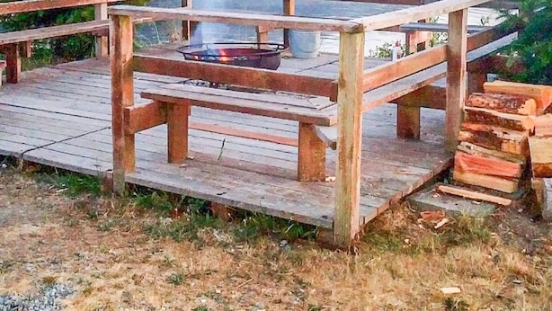 A wooden deck with a fire pit and benches, overlooking a lake and forested hills.