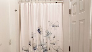 A bathroom with a shower curtain featuring floral designs, a white door, and a striped mat.