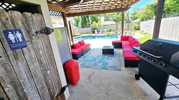 Une terrasse extérieure avec un barbecue, des sièges rembourrés de couleur rouge et une piscine en arrière-plan.