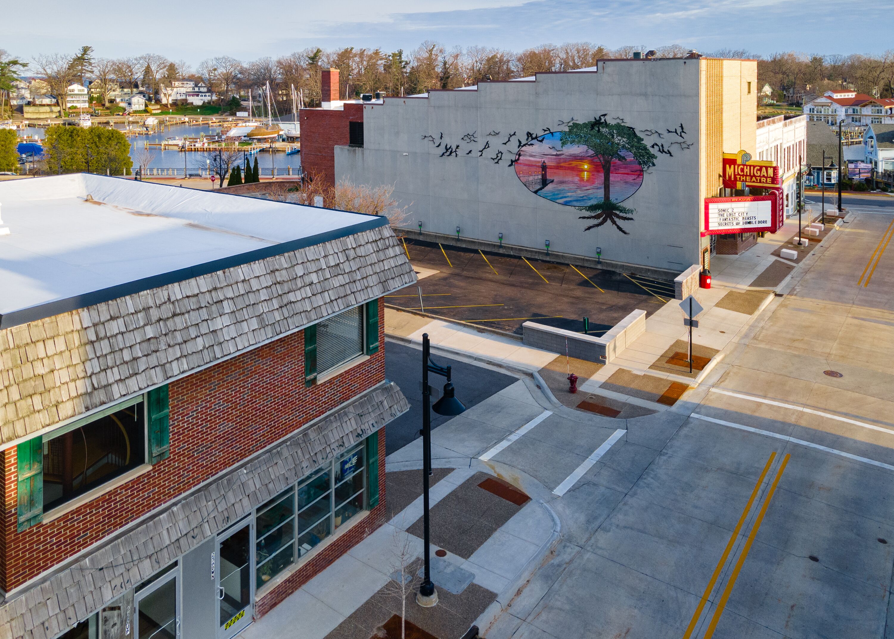A street view with a building featuring a mural of a tree and birds, a theater sign, and a parking lot.
