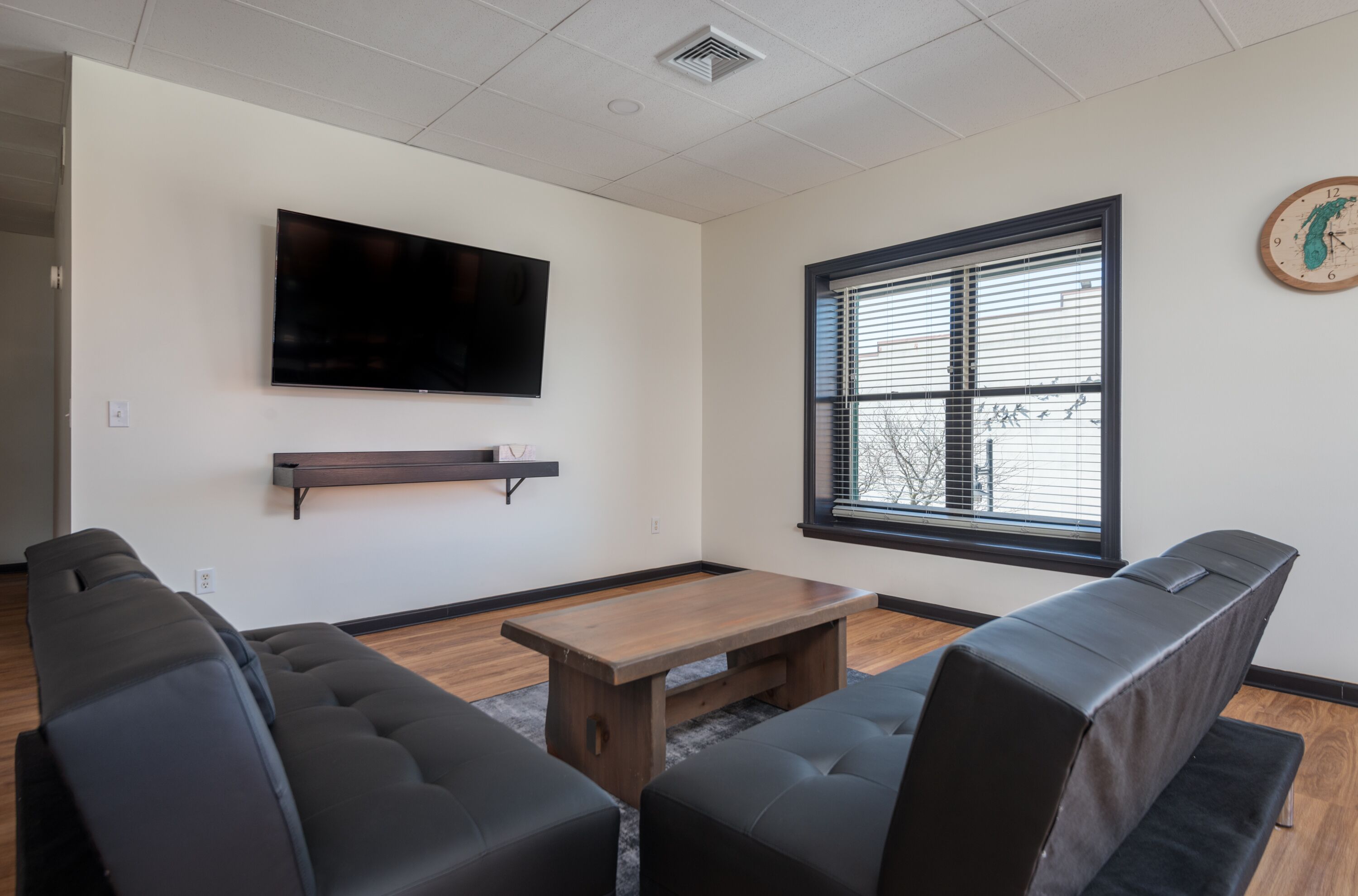 Un salon moderne avec un téléviseur à écran plat fixé au mur, une table basse en bois et des canapés en cuir noir.