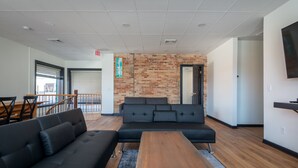 A modern lounge area with a black sectional sofa, a wooden coffee table, and a brick accent wall.