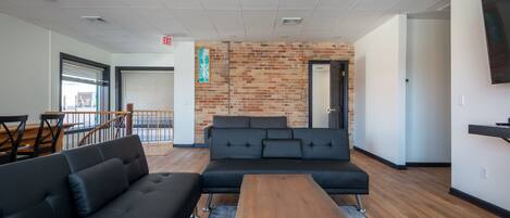 A modern lounge area with a black sectional sofa, a wooden coffee table, and a brick accent wall.
