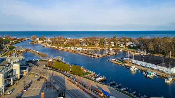 A marina with boats docked, a road leading to the marina, and buildings in the background.