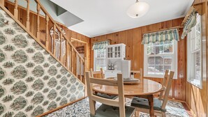Een kamer met houten lambrisering, een eettafel, stoelen en een trap met behangpapier met een patroon.