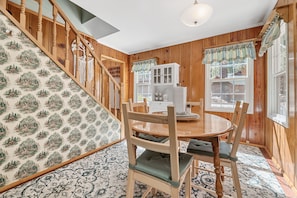 A wooden-paneled room with a dining table, chairs, and a staircase with a patterned wallpaper.