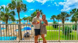 A couple standing on a balcony with a view of a beach, palm trees, and a pool area. - Beachfront Condo w/ FREE Beach Service, 2nd Floor, Pools, Saunas, Tootsie's (Panama City Beach)