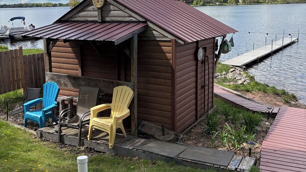 Una cabaña de madera con techo de metal, un muelle y una pequeña terraza con mobiliario exterior.