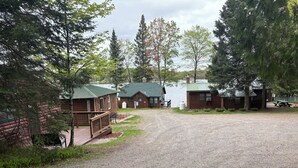 Un camping con cabañas de madera, un camino de grava y un lago al fondo.