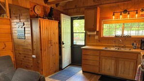 Un acogedor interior de cabaña con una mesa de comedor de madera, un sofá, una cocina con armarios de madera y un ventanal con vistas a la vegetación.
