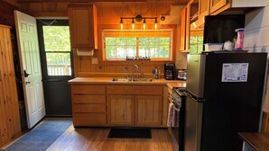 Una cocina compacta con armarios de madera, un refrigerador de acero inoxidable, una cafetera y un ventanal con vistas a zonas verdes.