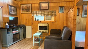 Interior acogedor de una cabaña con paredes de madera, un televisor, un sofá y cuadros en la pared.