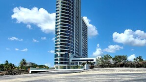 A tall, modern hotel with a curved facade, multiple balconies, and a clear blue sky in the background. - Lovely condo with beach, mountain and pool view. (Nueva Gorgona)