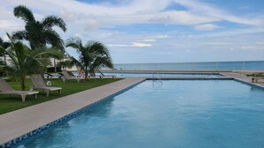 A swimming pool with lounge chairs and palm trees, surrounded by a clear sky. - Lovely condo with beach, mountain and pool view. (Nueva Gorgona)