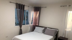 Une chambre à coucher avec un lit, des rideaux, une table de chevet et une fenêtre.
