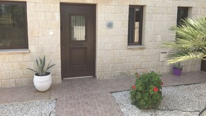 A stone building with a tiled roof, a dark brown door, and a small window. There are potted plants and a gravel pathway in front. - Beautiful detached villa with private pool. Sea & mountain views (Pissouri)