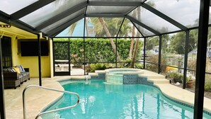 Ein überdachter Swimmingpool mit Glasbarriere, eine Lounge mit einer Couch und Blick auf Grünflächen.