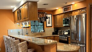 Eine moderne Küche mit Holzschränken, Edelstahlgeräten, einer Granitabdeckung und einer Bar mit Korbstühlen.