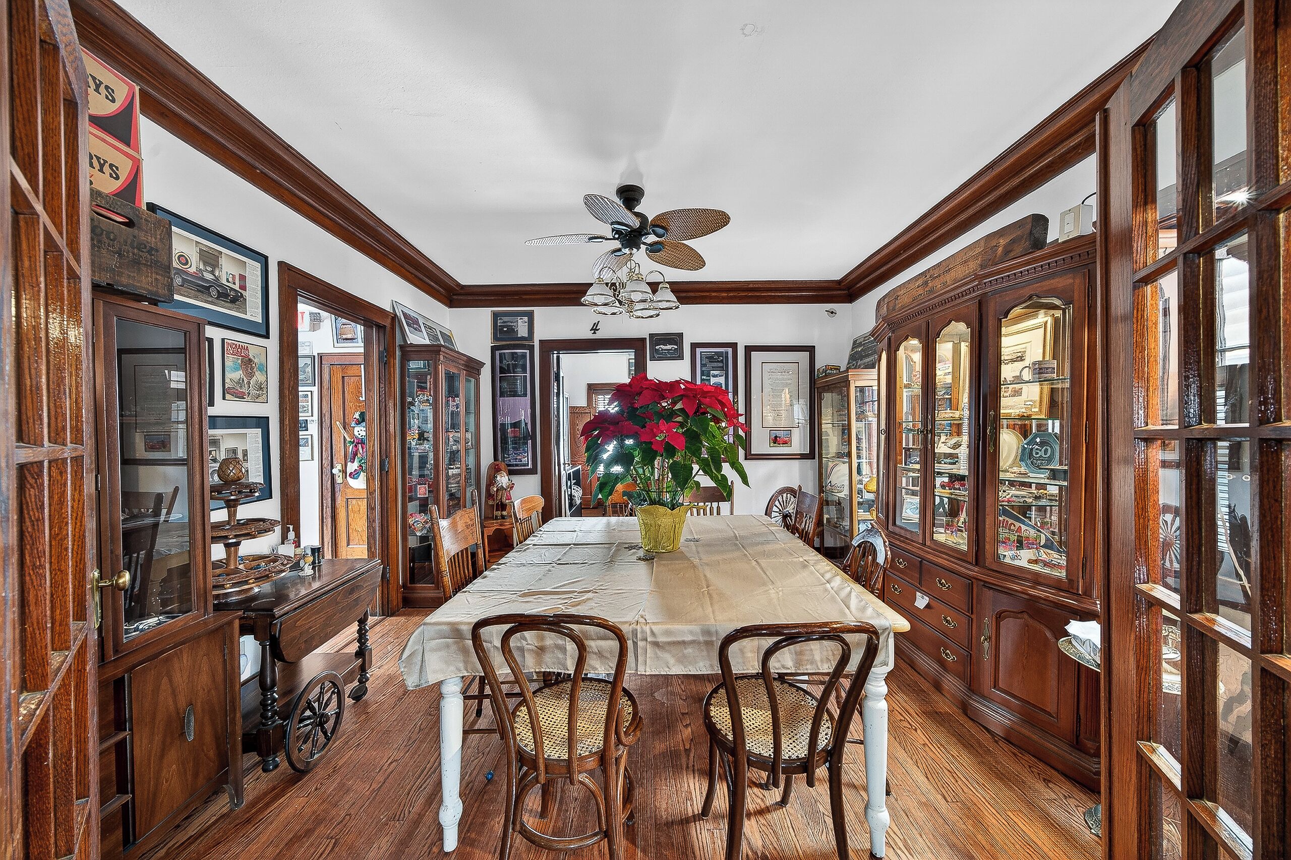 A dining room with a long wooden table, chairs, a ceiling fan, and wooden cabinets with glass doors.