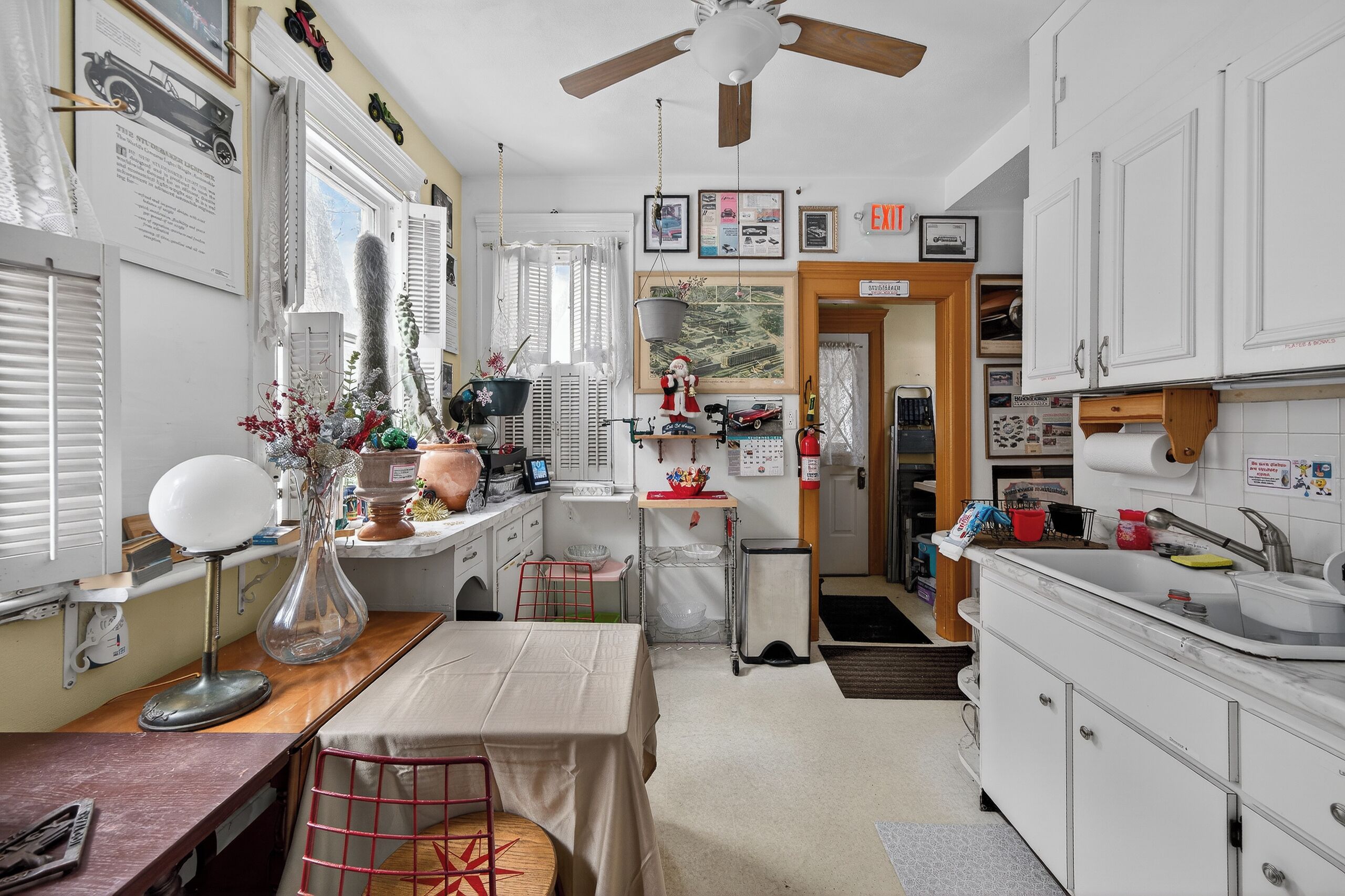 A compact kitchen with white cabinets, a dining table, and a ceiling fan.