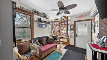 A cozy room with a wicker sofa, a small table, a ceiling fan, and a staircase leading to an upper level.