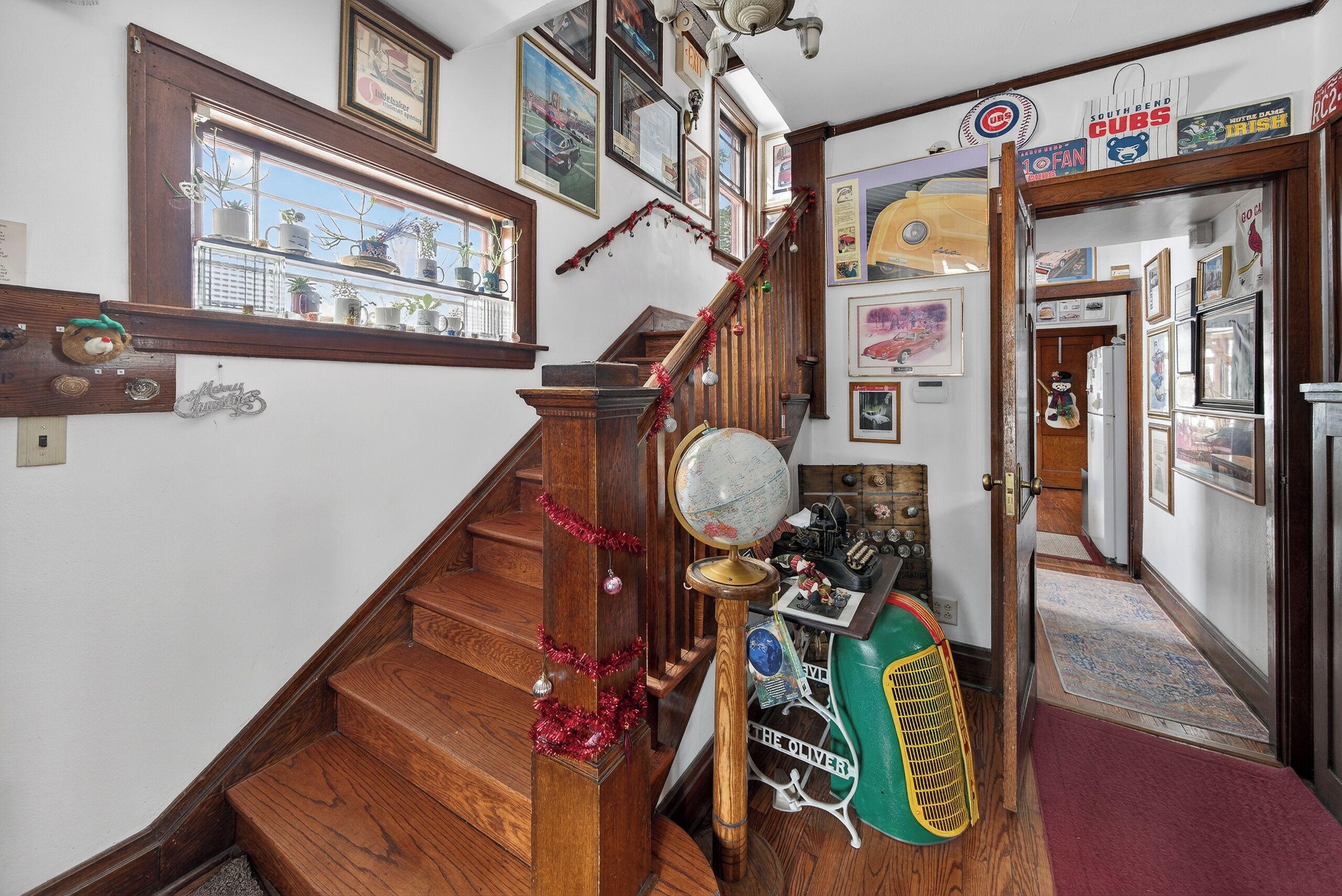 Un escalier en bois orné d’un globe terrestre et d’un ventilateur ancien, le tout décoré de guirlandes de Noël.