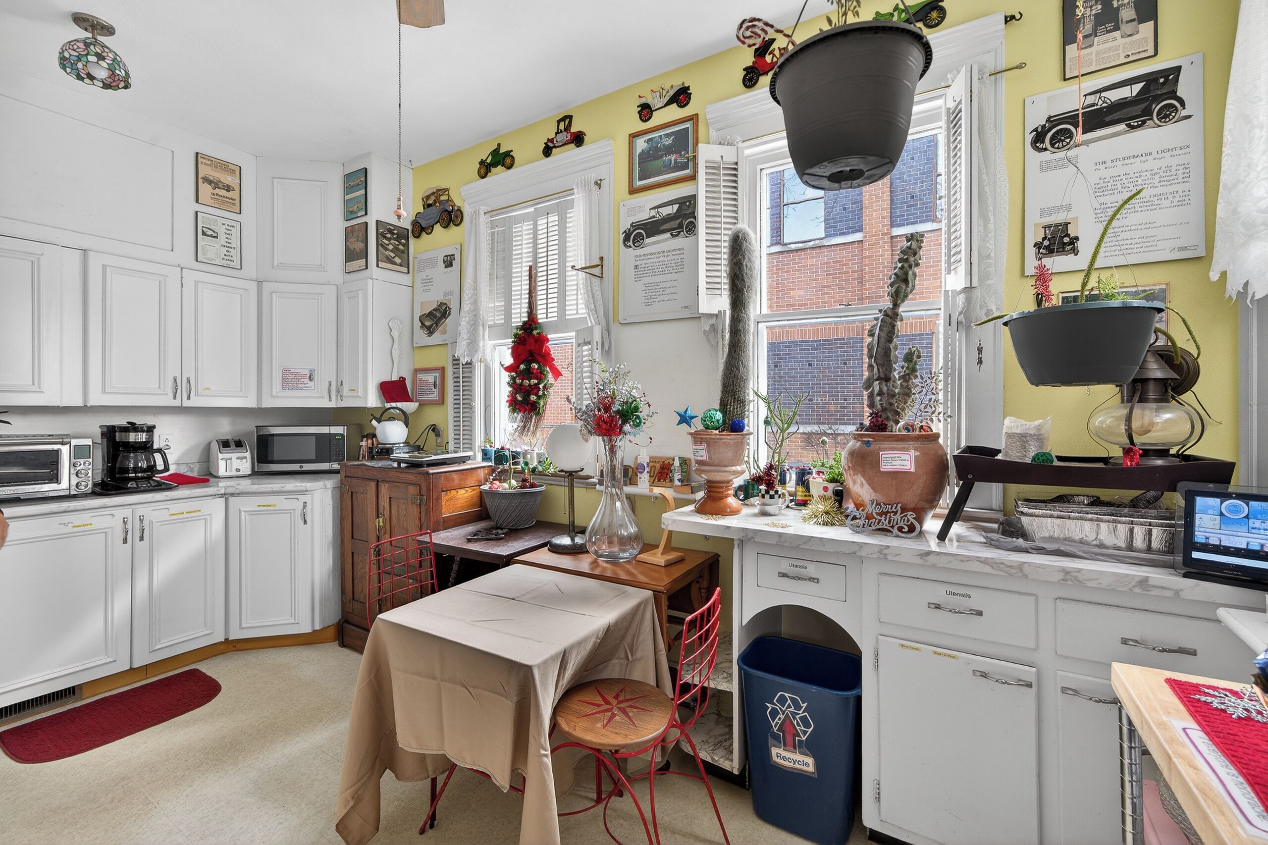 A kitchen with white cabinets, a dining table, and a red chair. There is a trash bin and a recycling bin.
