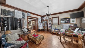 A cozy living room with a wooden floor, a sofa, a coffee table, and a dining table with chairs. There are framed pictures on the walls and a television on the wall. - The Avanti Houses (South Bend)