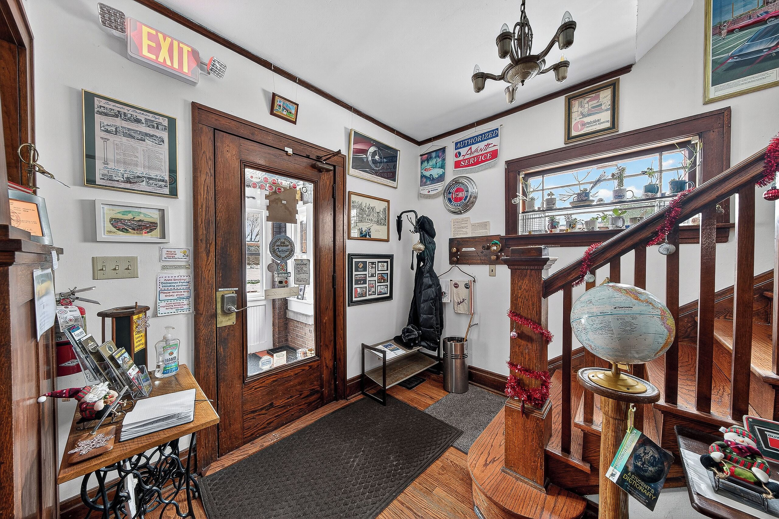 A hallway with an exit sign, framed pictures, a globe, and a staircase.