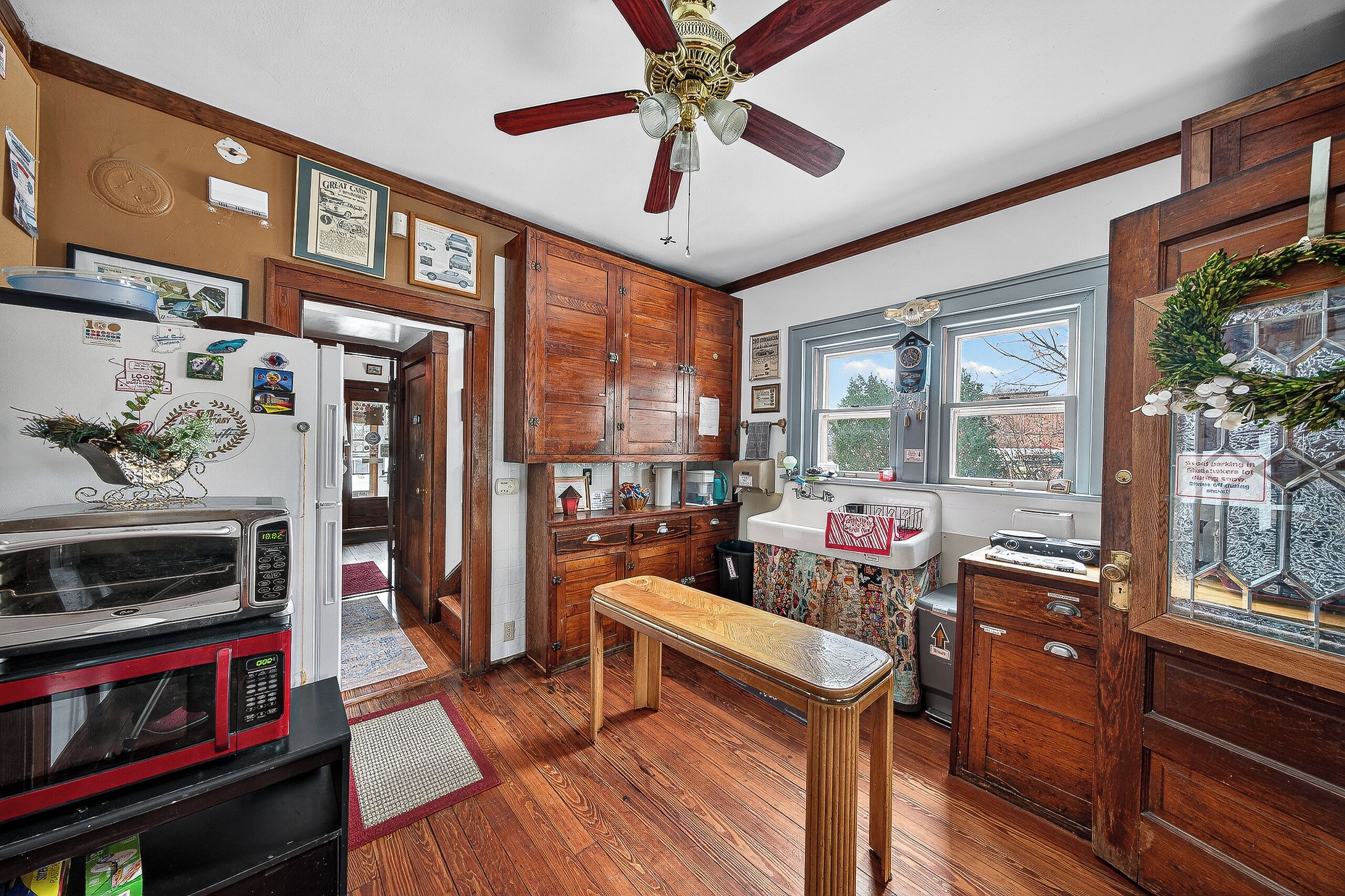 A kitchen with wooden cabinets, a ceiling fan, a refrigerator, a microwave, and a window with a view.
