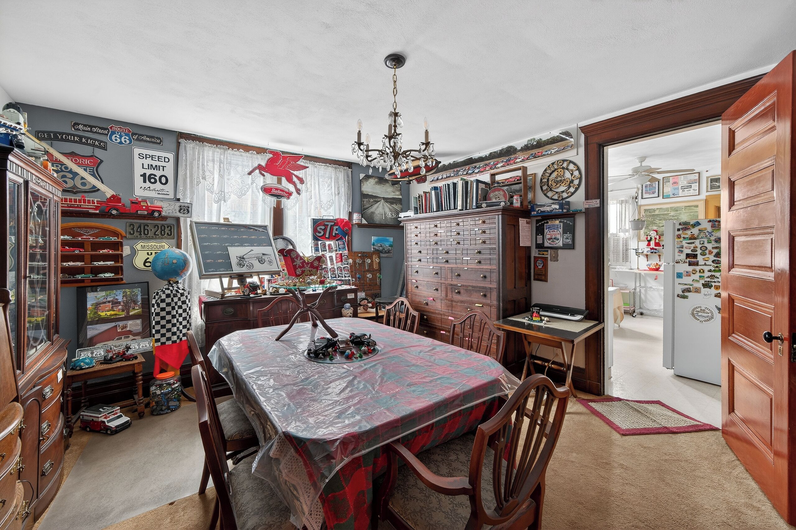 A room with a dining table, chairs, a chandelier, a clock, and various memorabilia on the walls.