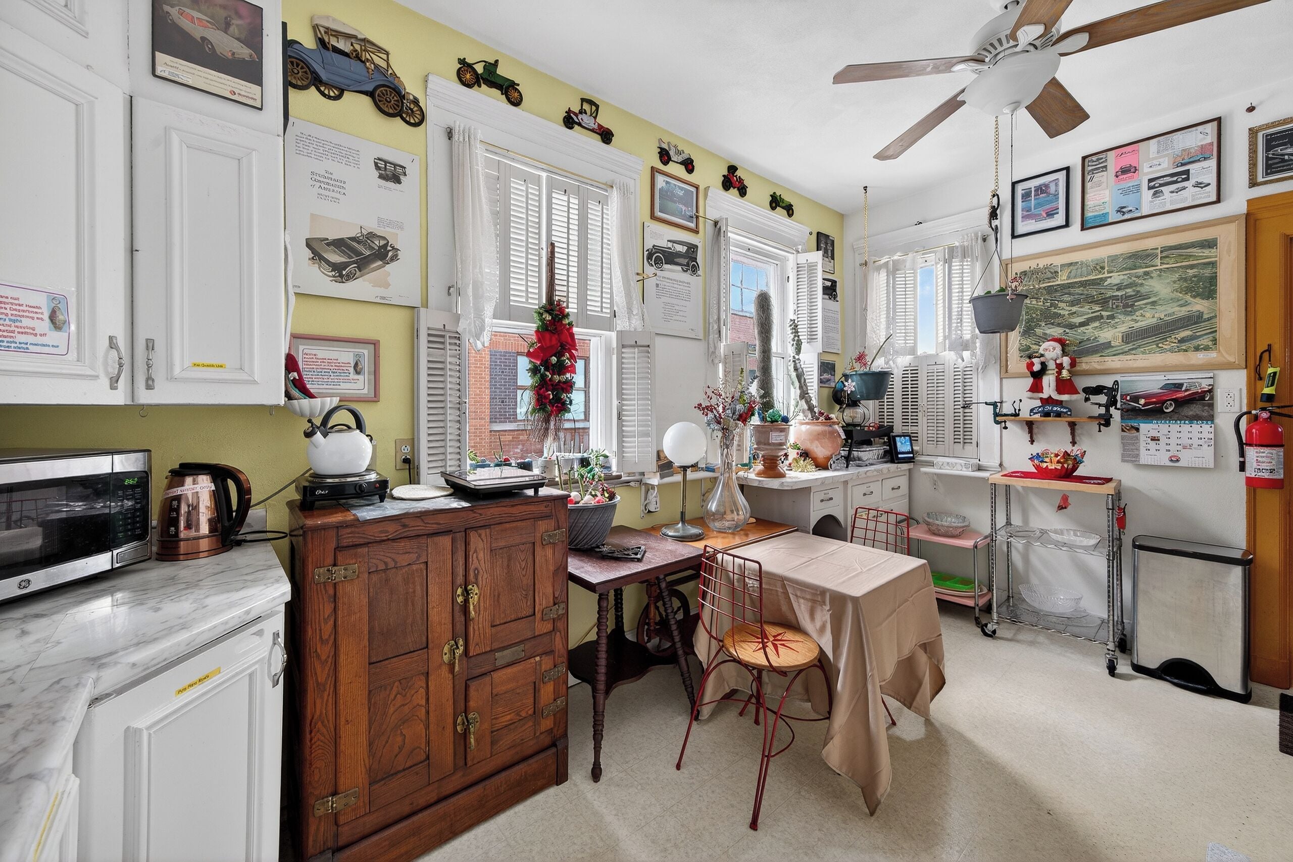 Une cuisine avec des armoires blanches, une armoire en bois, une table à manger avec une chaise et un ventilateur de plafond.