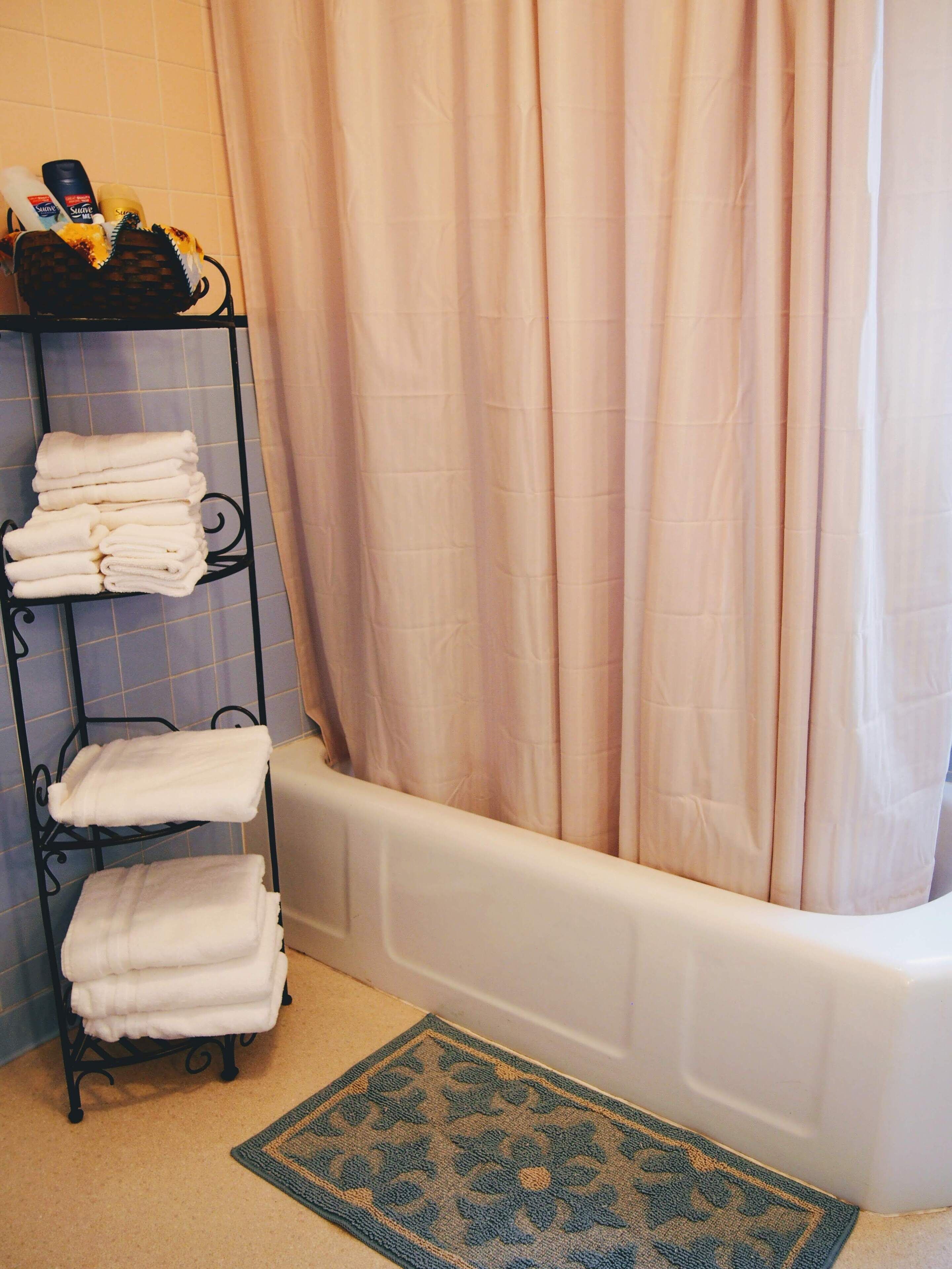 A bathroom with a bathtub, a towel rack with folded towels, and a shower curtain.