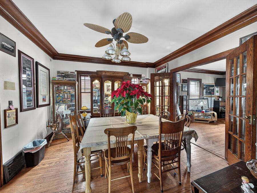 A dining room with a wooden table, chairs, a ceiling fan, and a potted plant.