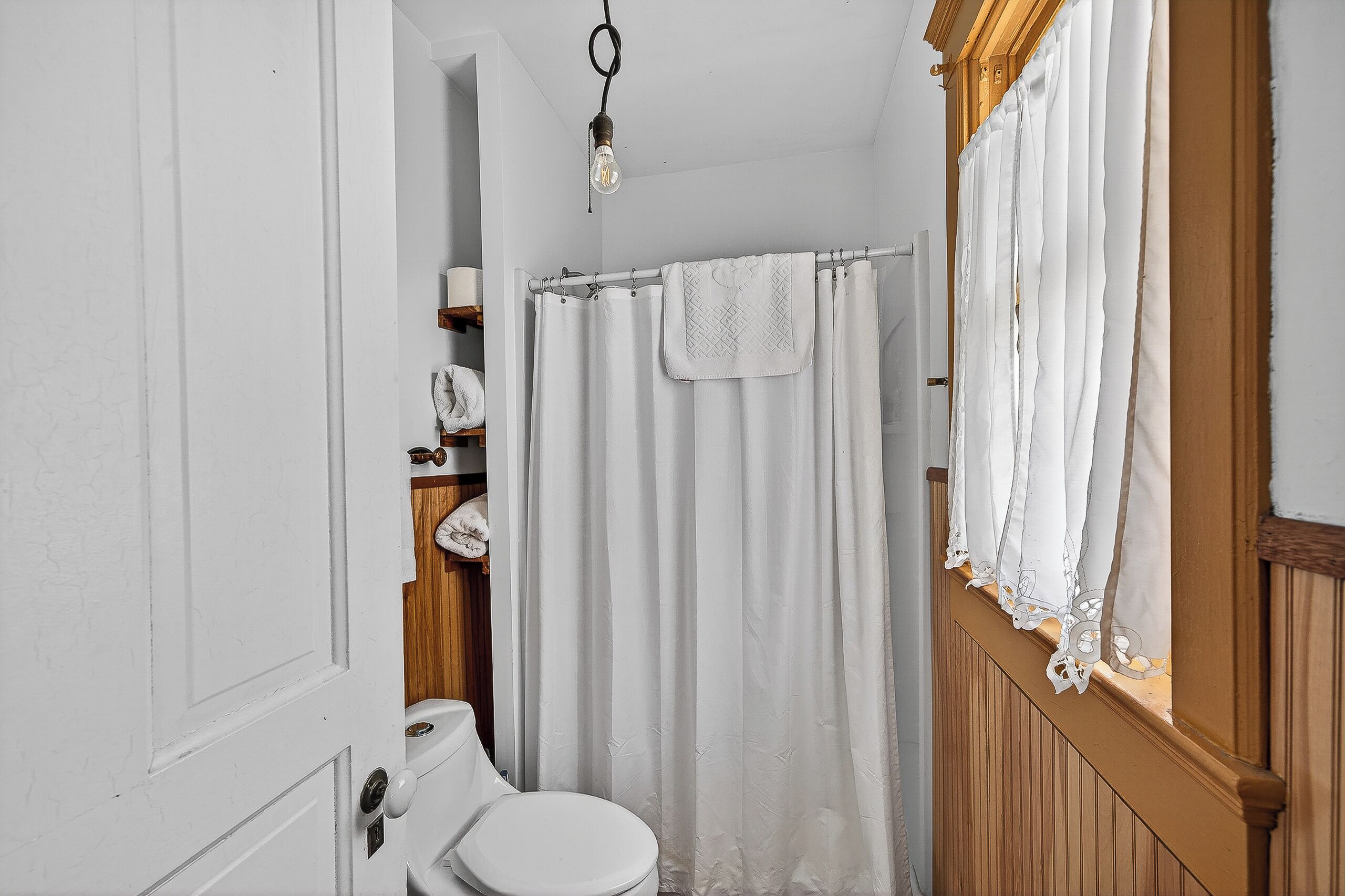 Un baño pequeño y blanco con un tocador de madera, inodoro blanco y cortina de ducha.