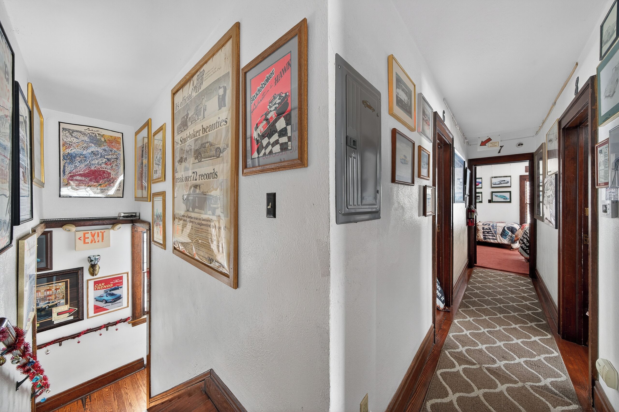 A hallway with framed automotive posters and a carpeted floor.