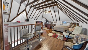 A loft-style bedroom with exposed wooden beams, a desk, two chairs, a bed, and a hanging light fixture. - The Avanti Houses (South Bend)