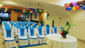 A conference room with rows of chairs, a round table with a white tablecloth, and a floral centerpiece. - Panchvati Comforts (Bengaluru)