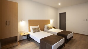 A hotel room with two single beds, a wooden wardrobe, a bedside table with a lamp, and a door. - Panchvati Comforts (Bengaluru)