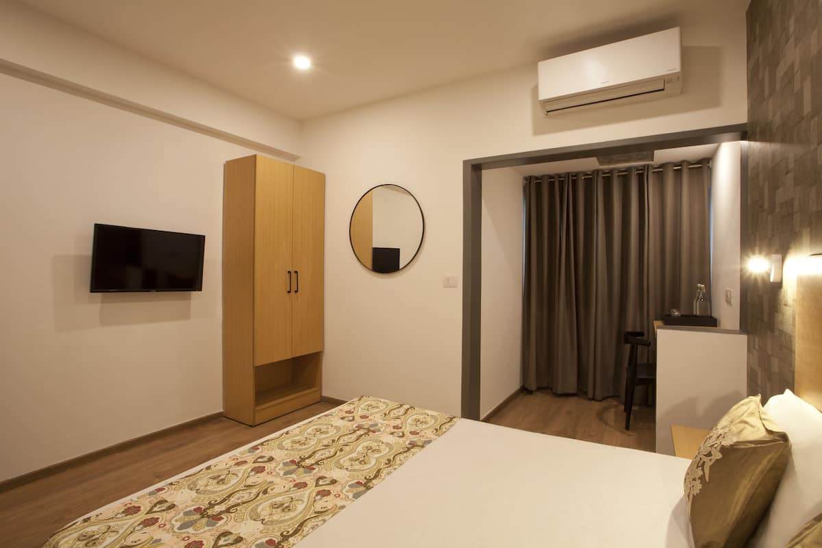 Une chambre d’hôtel moderne équipée d’un lit, d’une armoire, d’une télévision, d’un miroir et d’un appareil de climatisation.