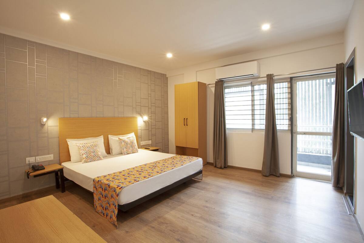 Une chambre d’hôtel moderne dotée d’un grand lit, d’une table de chevet, d’une commode, d’une armoire et d’une grande fenêtre avec des rideaux.