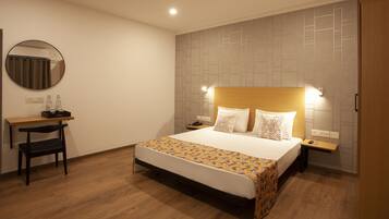 Habitación de hotel con cama, mesitas de noche, escritorio con silla, espejo redondo y pared con diseño geométrico.