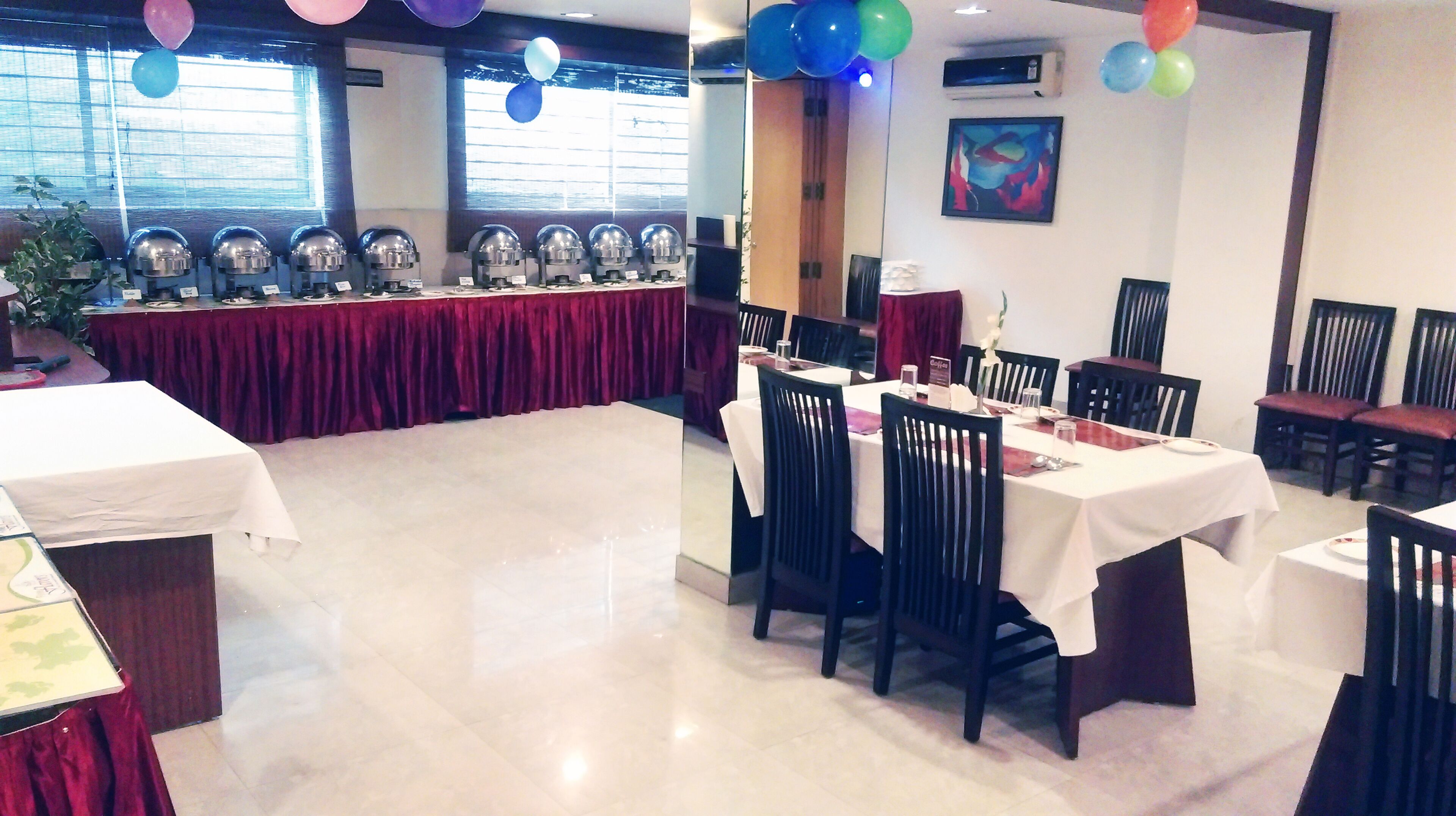 A banquet hall with tables set for dining, a stage with speakers, and balloons.