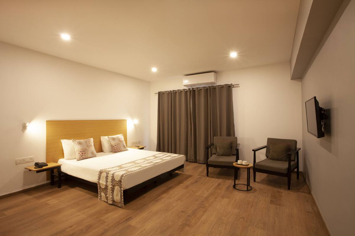 Une chambre d’hôtel avec un grand lit, deux fauteuils, une petite table, un téléviseur fixé au mur et un appareil de climatisation.