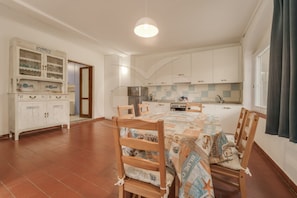 A compact kitchen with white cabinets, a central island, and a dining area with wooden chairs and a patterned tablecloth.