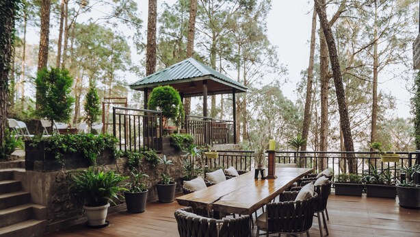 A wooden deck with a dining table and chairs, surrounded by potted plants and a gazebo.